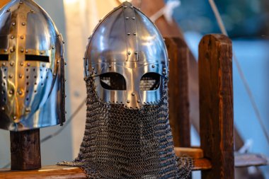 Two helmets, one of which is a knight's helmet, are displayed on a wooden stand. The knight's helmet is made of metal and has a mesh-like design. The other helmet is a smaller, more decorative piece clipart