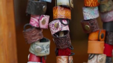 Farklı renkte ve tasarımlarla birlikte asılı bir sürü deri bilezik. Bilezikler deriden yapılmıştır ve çiçekler ve girdaplar da dahil olmak üzere farklı tasarımları vardır.