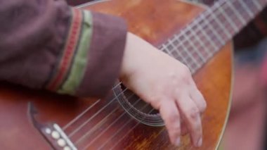 Bir kişi kahverengi bir vücutla gitar çalıyor. Gitar eski ve klasik bir görünüme sahip. Kişinin eli gitarın üzerinde, ve resim nostaljiyi ve müziğin güzelliğini yansıtıyor.