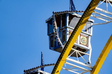 Gökyüzünde mavi-beyaz vagonlu bir dönme dolap var. Vagon dönme dolabın tepesinde yer almaktadır ve aracın görünen tek kısmı da burasıdır.