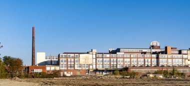 Uzun bacalı büyük bir tuğla bina. Gökyüzü açık ve mavi. Bina eski ve terk edilmiş.