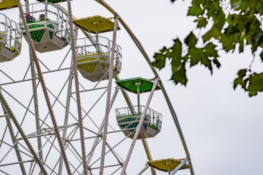 Renkli koltukları olan büyük bir dönme dolap. Tekerlek bir ağaç ve gökyüzü ile çevrilidir.