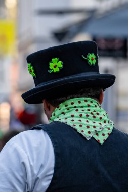 Siyah şapkalı, yeşil ve kırmızı eşarplı bir adam. Şapkada yeşil bir yonca var.