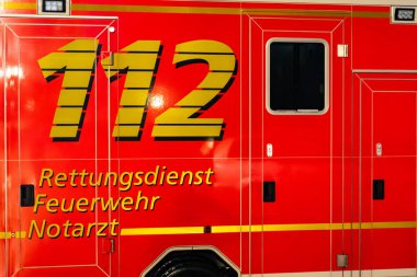 Üzerinde 112 yazan kırmızı ve sarı bir ambulans. Ambulans garajda bekliyor.