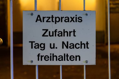 Alman dilindeki bir işaret insanları geceleri izinsiz girmemeleri konusunda uyarıyor. İşaret beyaz ve siyah ve bir çite bağlı.