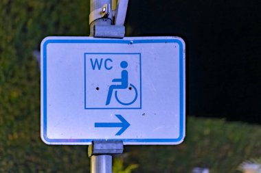 Tekerlekli sandalye sembolü ve solu gösteren mavi bir ok. Tabela direğin üstünde.