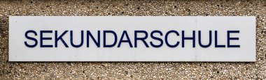 Üzerinde Sekundarschule yazan bir tabela. İşaret mavi ve beyaz.