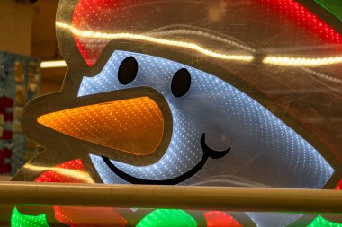 Havuç burunlu ve gülen yüzlü bir kardan adam. Kardan adam ışıklarla çevrili ve mutlu.