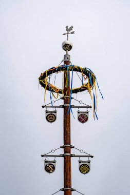 Tepesinde rüzgar gülü ve ortasında çelenk olan uzun bir direk. Çelenk kurdelelerle kaplı ve çeşitli renklere sahip.