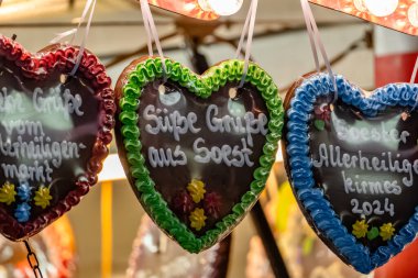 Üzerinde farklı renkte krema ve yazı olan üç kalp şeklinde kurabiye. Yazı Almanca 