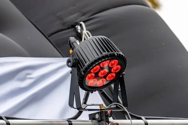 Üzerinde kırmızı ışıklar olan siyah bir ışık, siyah bir arka plana doğru aydınlatılır. Işıklar dairesel bir düzende dizilmiş, her ışık farklı bir renk yayıyor.