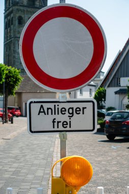 Üzerinde Anlieger Frei yazan kırmızı beyaz bir tabela. Tabela bir direğin üzerinde ve bir binanın önünde.