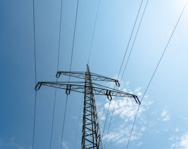 A tall power line tower is seen against a blue sky. The sky is clear and the sun is shining clipart