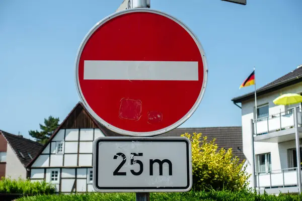 Siyah kenarı ve beyaz numarası 25 olan kırmızı beyaz bir tabela. Tabela bir evin önündeki direğin üzerinde.