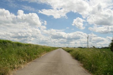 Arka planda uzun bir yel değirmeni olan bir yol. Gökyüzü bulutlu ve güneş parlıyor