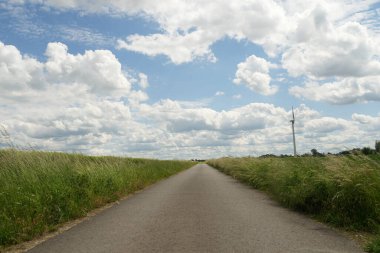 Gökyüzünde birkaç bulut olan bir yol. Gökyüzü mavi ve bulutlar beyaz