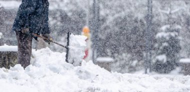 Bir adam kaldırımdan kar kürüyor. Kar üst üste yığılmış ve adam onu temizlemek için bir kar küreği kullanıyor. Sahne soğuk ve karlı, ve adam karı temizlemek için çok çalışıyor.
