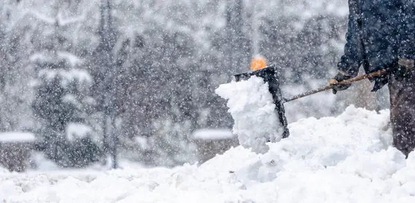 Bir adam kaldırımdan kar kürüyor. Kar birikiyor ve adam temizlemek için kürek kullanıyor. Sahne soğuk ve karlı, adam karı temizlemek için çok çalışıyor.