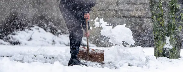 Bir adam kar küreme aracıyla kar kürüyor. Kar yağıyor ve adam siyah bir ceket giyiyor.