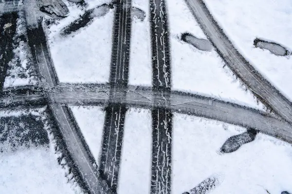 Lastik izleri ve siyah çizgileri olan karlı bir yol. Sahne biraz ürkütücü.