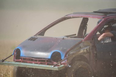 Bir araba tarlanın ortasında ve içinde bir insan var. Araba ezilme sürecinde.