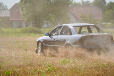 Bir araba toprak tarlasının içinden geçiyor. Araba siyah ve üzerinde bir sürü çamur var. Araba düz bir çizgide gidiyor ve o hızlı gidiyor. Alan kuru ve tozlu.