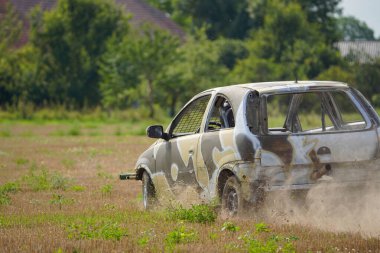 Bir araba çimlerin ve toprağın içinden geçiyor. Araba çamurla kaplı ve kamuflaj deseni var.