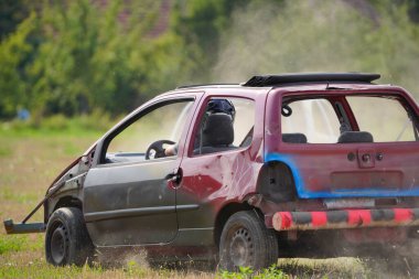 Bir araba hurdalıkta, içinde bir adam var. Araba kırmızı ve çok fazla hasar var.