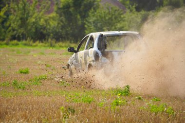 Bir araba, toz ve molozlardan oluşan bir arazide ilerliyor. Araba çamurla kaplı ve o bir yarışta. Sahne kaotik ve yoğun.