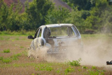 Bir araba toprak ve çimlerin arasından geçiyor. Arabanın üstü kir içinde ve ön tarafı hasarlı. Olay yeri kaotik ve düzensiz. Arkasında toprak izi bırakıyor.