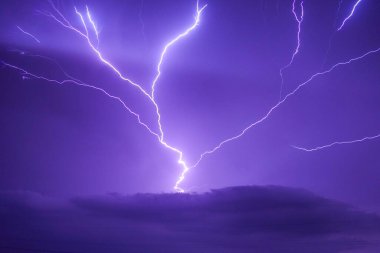 Ortasında yıldırım olan mor bir gökyüzü. Gökyüzü karanlık ve fırtınalı. Yıldırım uzun ve parlak.