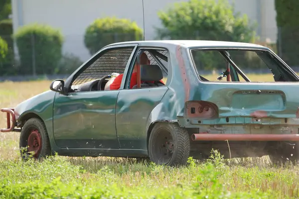Kırık ön camlı yeşil bir araba ve sürücü koltuğunda bir adam. Araba ya hurdalıkta ya da hurdalıkta.