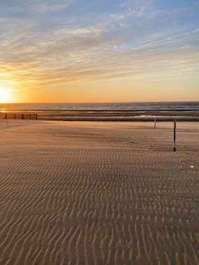 Sahilde sıcak akşam ışığı, dalgalı kum ve uzak deniz