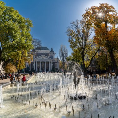 Sofya, Bulgaristan - 30 Ekim 2022: Sofya şehir merkezindeki Şehir Bahçesinde fıskiye ve arka planda Ulusal Tiyatro binası