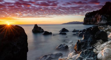 Cala Gonone 'da renkli bir gün doğumu. Siyah beyaz kayalar ve kayalar ve güneş ışığı.