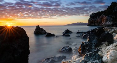 Cala Gonone 'da renkli bir gün doğumu. Siyah beyaz kayalar ve kayalar ve güneş ışığı.