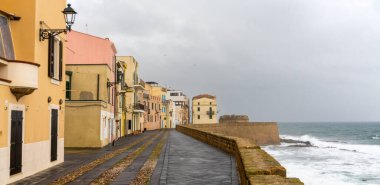 Alghero, İtalya - 14 Aralık 2022: Fırtınalı bir bulutlu gökyüzü altında Alghero 'da surları ve savunmaları güçlendirilmiş tarihi liman manzarası