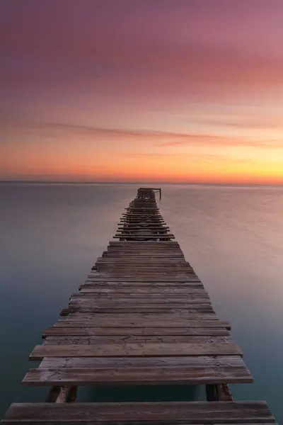 stock image A vertical sunrise seascape with an old wooden dock leading out into the calm ocean waters