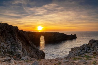 Günbatımında Menorca Adası 'ndaki Pont d' en Gil 'in taş kemerinin manzarası.