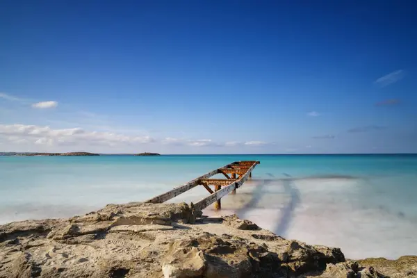 An old dock leads out into the turquoise waters of the Ses Illetes Beach in northern Formentera