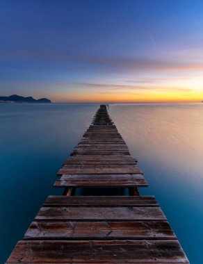 Sakin okyanus sularına açılan eski ahşap bir rıhtımla dikey bir gündoğumu deniz manzarası.