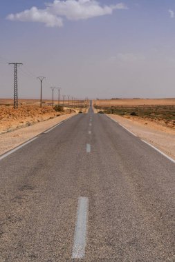 Fas 'ın güneybatısındaki kaya ve kum çöllerinden geçen sonsuz bir çöl otoyolu ve elektrik hatlarının dikey görüntüsü.
