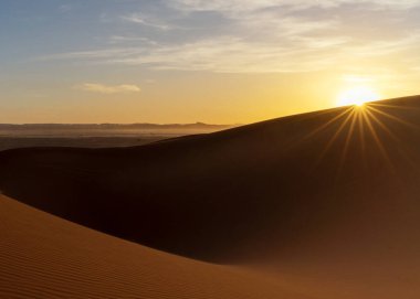 A view of the sand dunes at Erg Chebbi in Morocco at sunset with a sunstar clipart