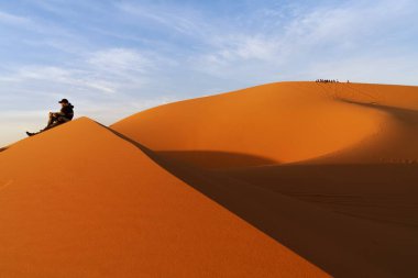 Merzouga, Fas - 9 Mart 2024: Erg Chebbi 'nin kum tepesinde tek başına oturan bir grup turist