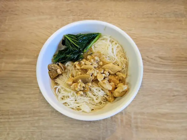 Tavuk dilimli buğulanmış pirinç vermicelli ve hafif çorba içinde canlı bok choy, ahşap bir yüzey üzerinde güzel bir kasede servis edilir.