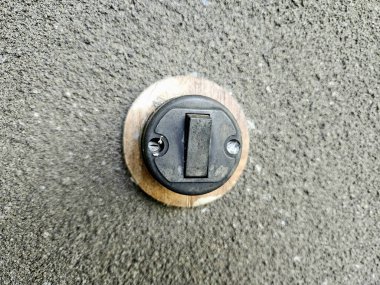 Köy cazibesi ve endüstriyel stili birleştirilmiş desenli beton bir duvara monte edilmiş ahşap tabanlı klasik siyah ışık anahtarı.