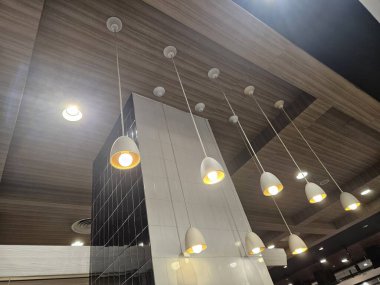 Endüstriyel dokunuşlu uzun beyaz kolye ışıkları, modern tavan tasarımına çağdaş bir bakış için bir sıra halinde sıcak altın ışık yayıyor.