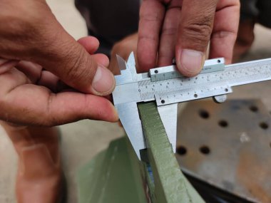 Metal kirişi ölçmek için kalibre kullanan ellerin yakın çekimi..