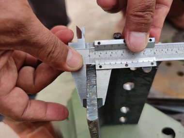 Metal kirişi ölçmek için kalibre kullanan ellerin yakın çekimi..