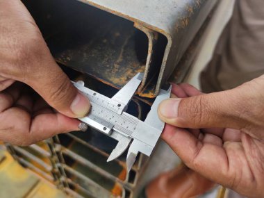 Endüstriyel amaçlar için paslı bir metal borunun boyutlarını ölçmek için kalibre kullanan ellerin yakın görüntüsü